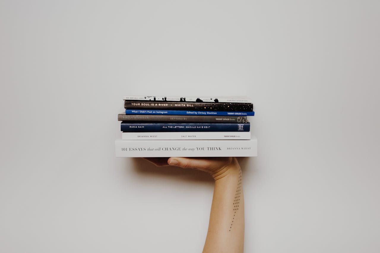 Hand holding a stack of books against a minimal white background, perfect for educational themes.